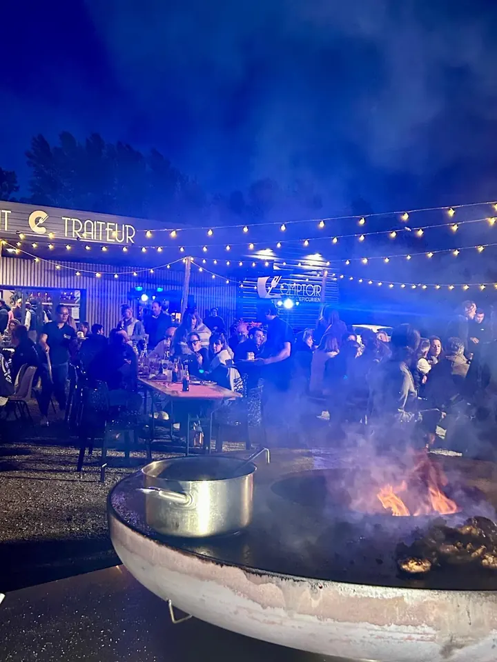 Soirée brasero : convives et fumée devant l'enseigne Traiteur illuminée