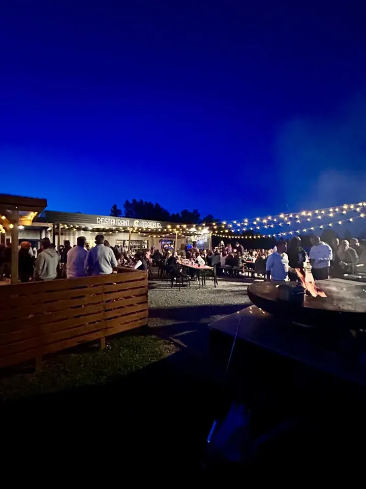 Terrasse du restaurant à la tombée de la nuit, brasero et guirlandes lumineuses sous un ciel bleu profond